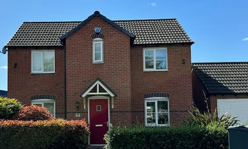 A red door and windows in front of a brick house.