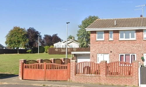 A brick house with a fence and trees in the background.